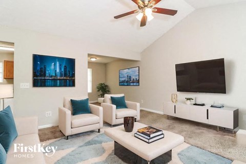 A living room with a white couch, a white coffee table, a white chair, a white TV stand, a ceiling fan, and a painting on the wall.
