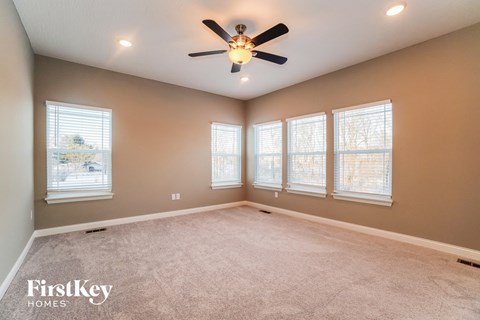 an empty living room with a ceiling fan and three windows
