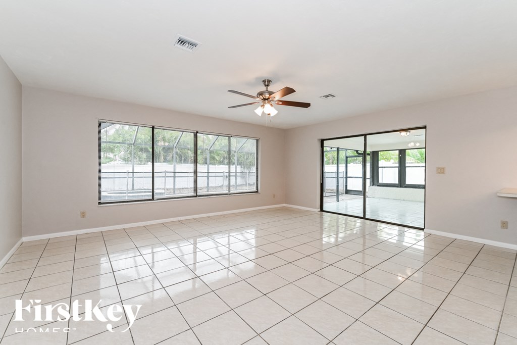 an empty living room with large windows and a ceiling fan