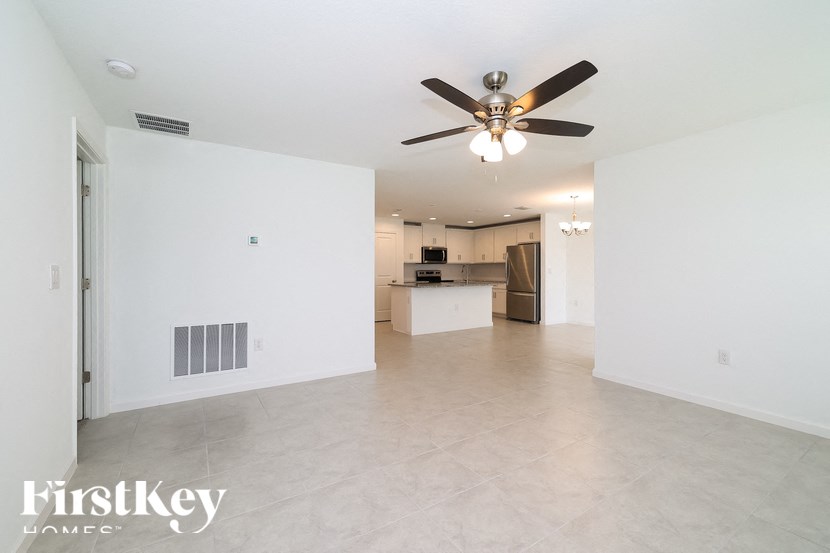 A spacious, empty room with a ceiling fan and a kitchen in the background.