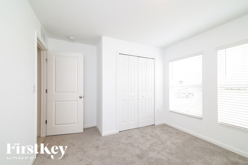 A white room with a door, a window with blinds, and a carpeted floor.