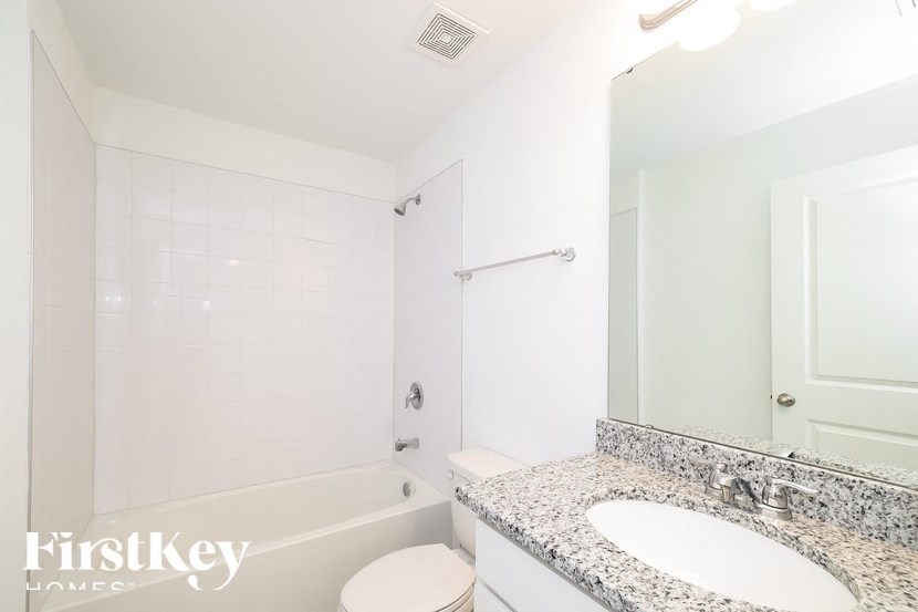 A white bathroom with a granite counter top and a walk in shower.