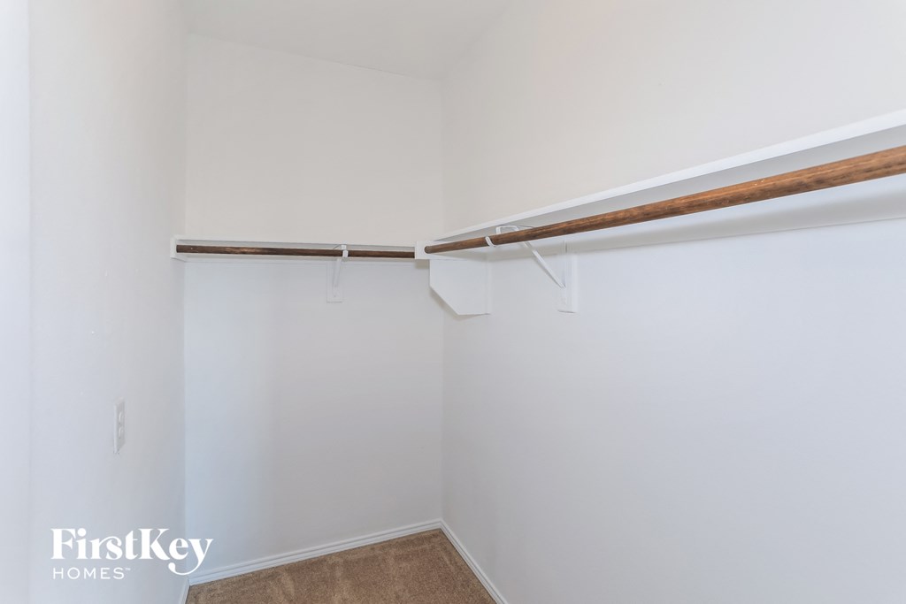 a walk in closet with white walls and a wooden rail on the ceiling