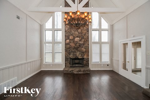A large, empty room with a stone fireplace and wooden floors.
