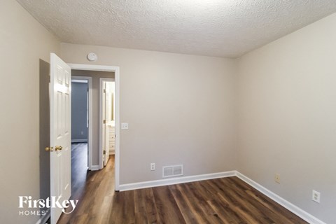 a bedroom with hardwood flooring and white walls and a door to a hallway