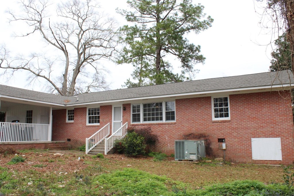 the front of a brick house with a white porch and some trees