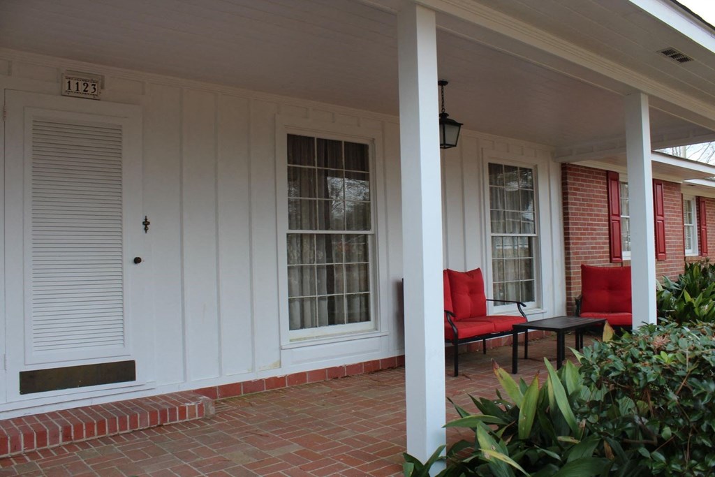the front porch of a home with red chairs and a table