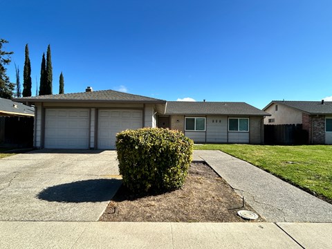 A house with a white garage door and a green bush in front.