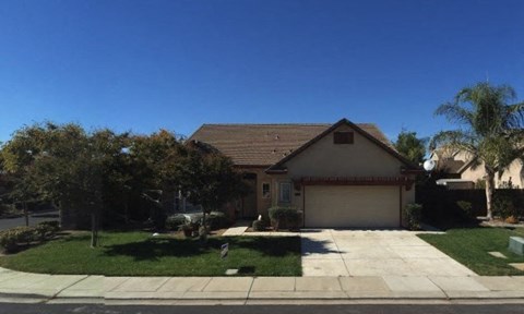 A house with a brown roof and a garage door is surrounded by a well-manicured lawn and trees.
