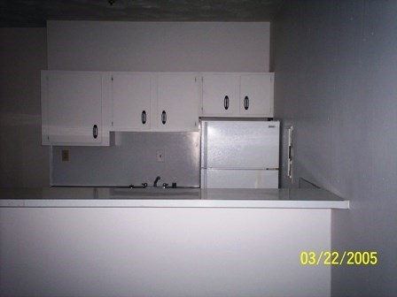 an empty kitchen with white cabinets and a refrigerator