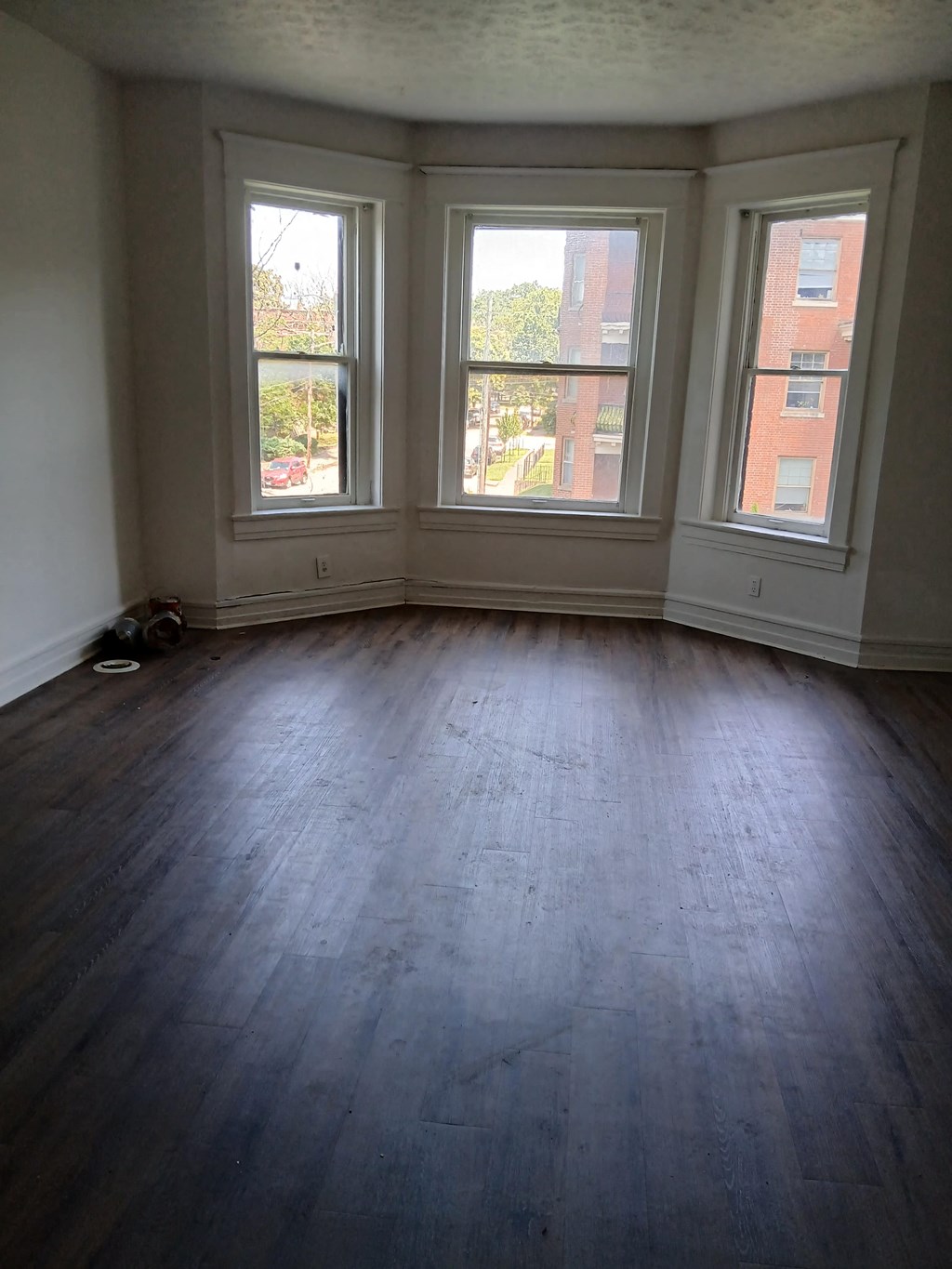 the living room of a house with wood floors and three windows