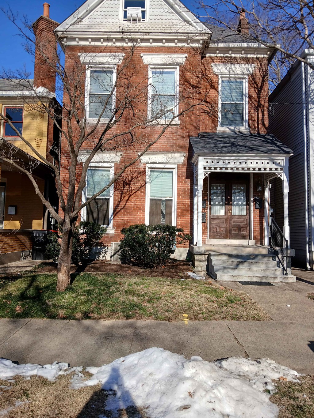 A red brick house with a tree in front.