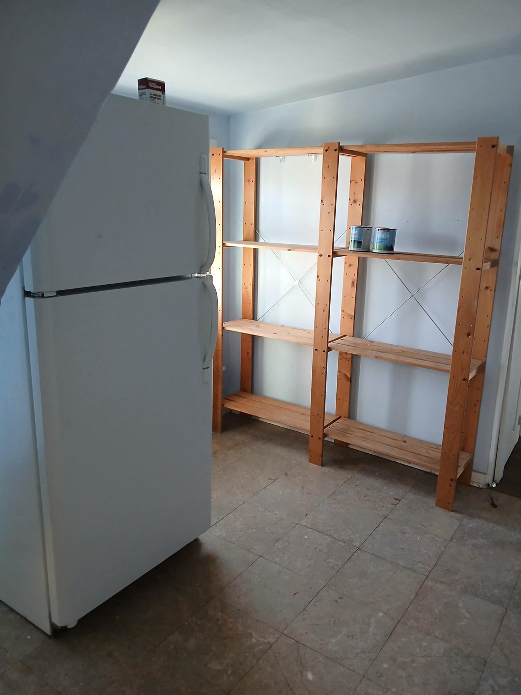 A white refrigerator is in a kitchen with a wooden framing structure in the background.