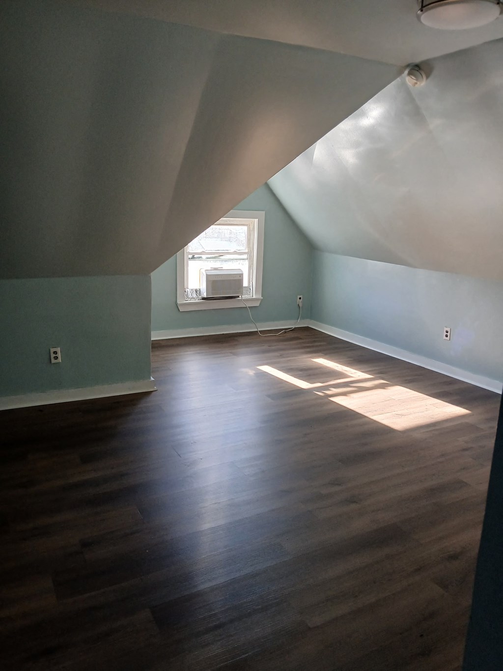 A room with wooden floors and a window letting in sunlight.