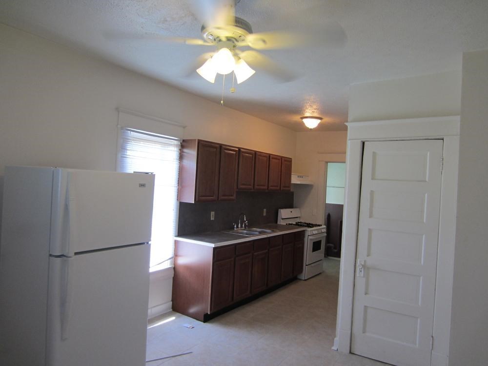 an empty kitchen with a refrigerator and a ceiling fan
