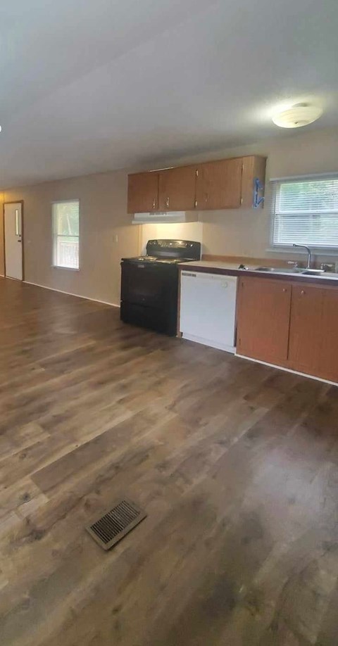 A kitchen with wooden floors and a black fridge.