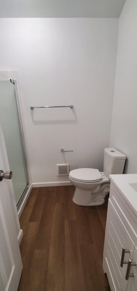 A white toilet in a small bathroom with wood flooring.