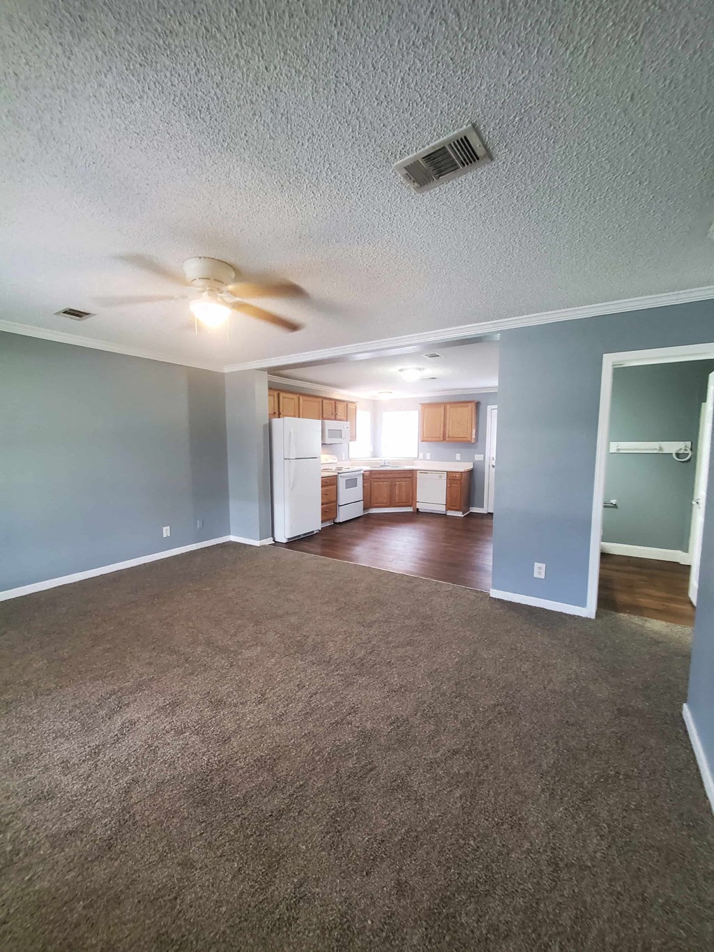 an empty living room with a ceiling fan and a kitchen