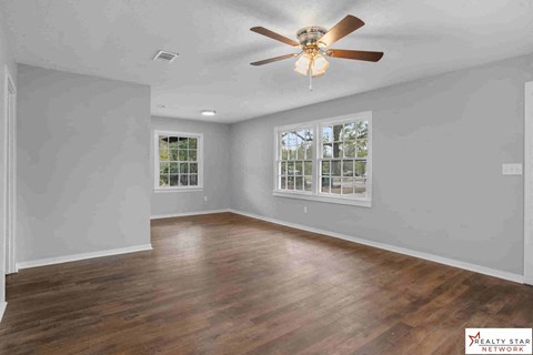 A spacious room with a ceiling fan and wooden flooring.