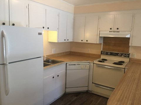 A white refrigerator is in a kitchen with white cabinets.