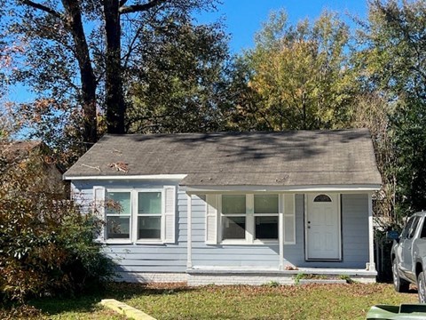 A small house with a white door and windows is surrounded by trees.