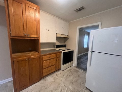 A kitchen with a white fridge, wooden cabinets and a window.