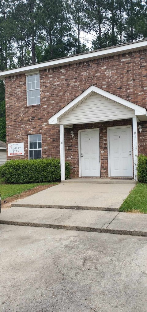 A brick house with a white door and a sign in front.
