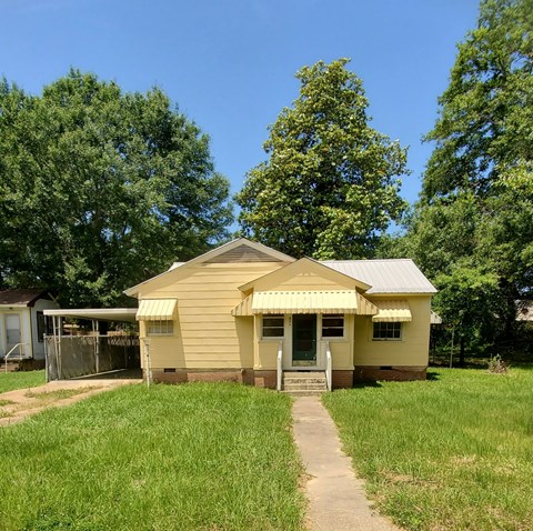 A small yellow house with a metal roof and a porch.
