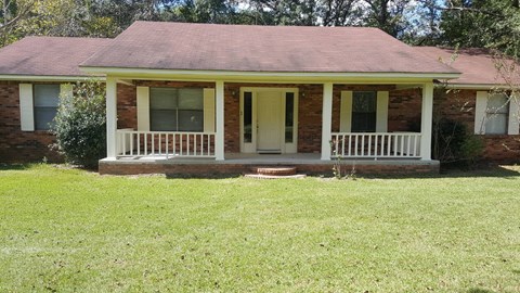 a small brick house with a porch and a lawn