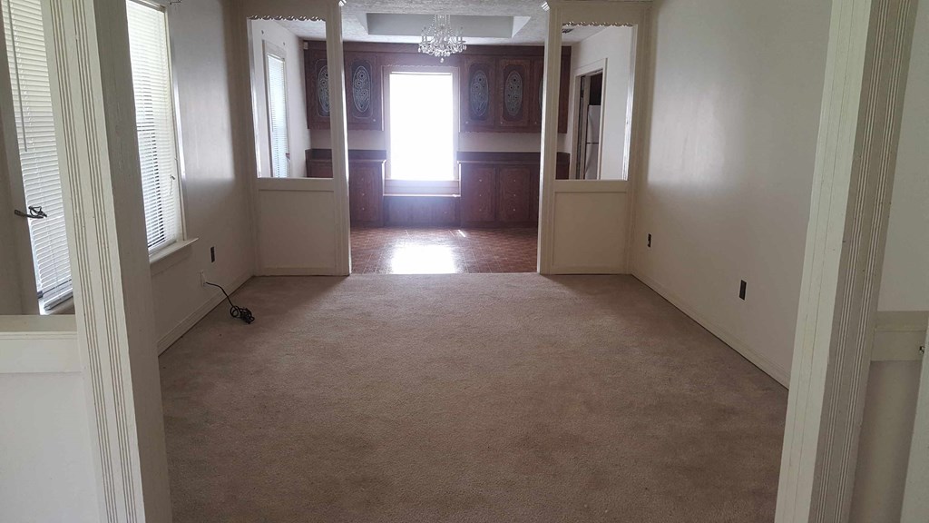 an empty living room with a carpeted floor and a door to a bedroom