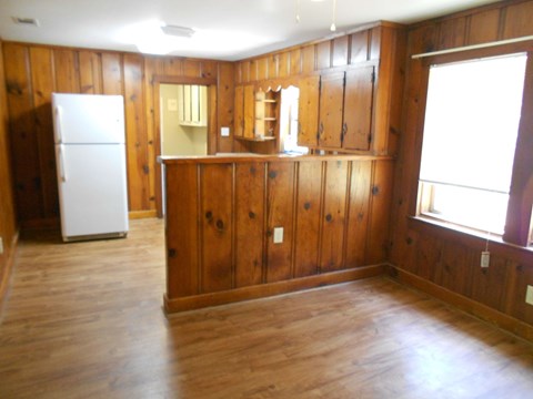 an empty living room with wood paneling and a refrigerator