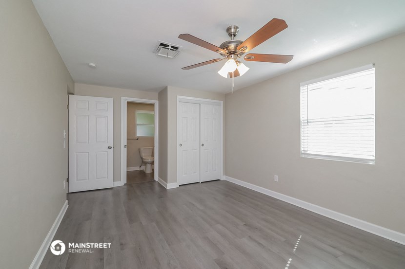 an empty living room with a ceiling fan and a door to the bathroom