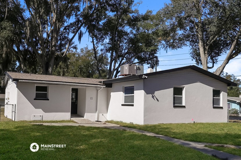 the front of a white house with a lawn and trees