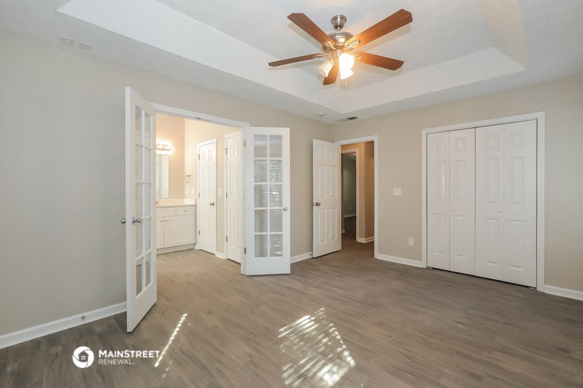 an empty living room with a ceiling fan and white doors