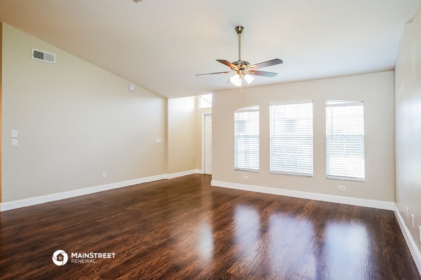 an empty living room with a ceiling fan and windows