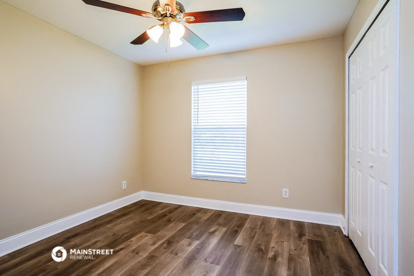 the spacious living room with hardwood flooring and a ceiling fan
