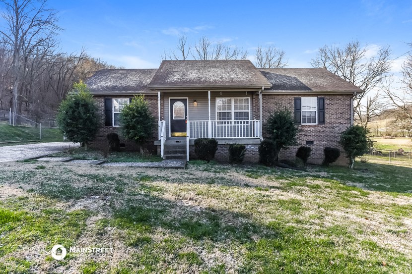 the front of a brick house with a white porch and a lawn