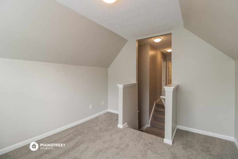 the upstairs bedroom has carpeted floors and white walls and a staircase