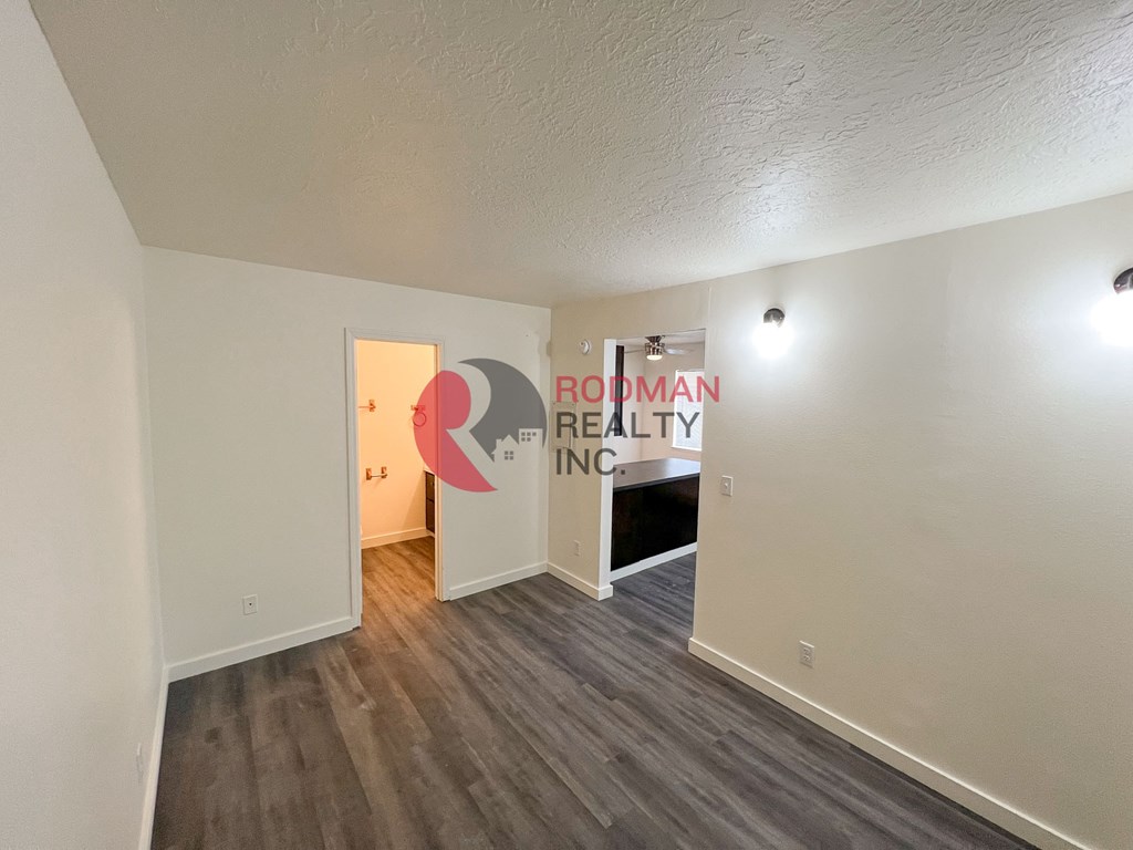 A room with a wooden floor and a white wall with a doorway leading to another room.