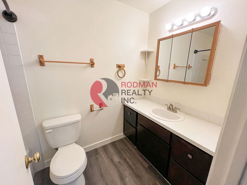 A white toilet sits in a bathroom with a wooden cabinet and a mirror above it.