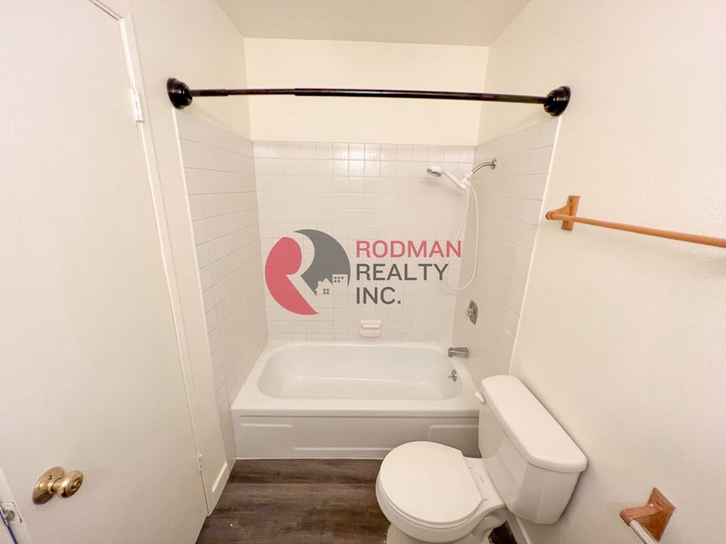 A white toilet sits in a bathroom with Rodman Realty Inc. on the wall.