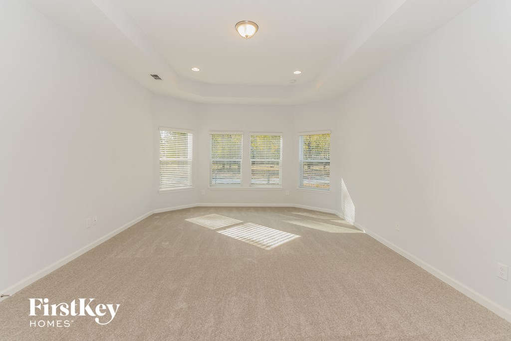 A spacious empty room with a carpeted floor and a window with blinds.