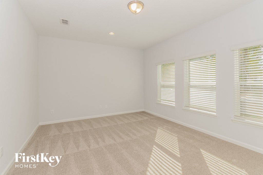 A room with a carpeted floor and two windows with blinds.