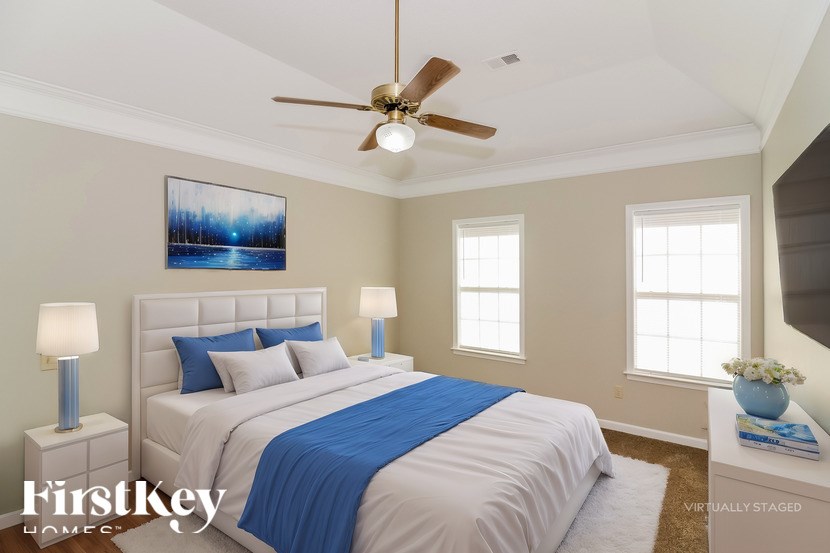 A bedroom with a bed, two lamps, a ceiling fan, and a painting on the wall.