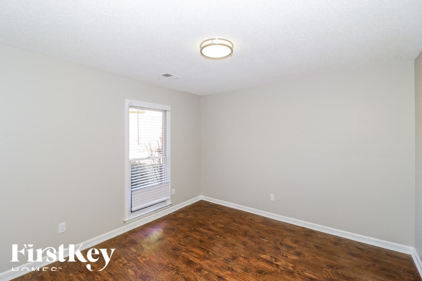 a bedroom with a hardwood floor and white walls and a window
