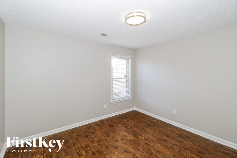 a bedroom with wood flooring and white walls and a window