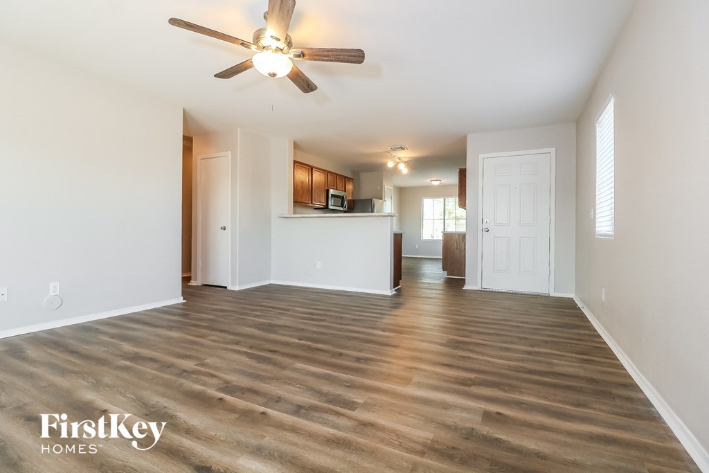 an empty living room with a ceiling fan and a kitchen