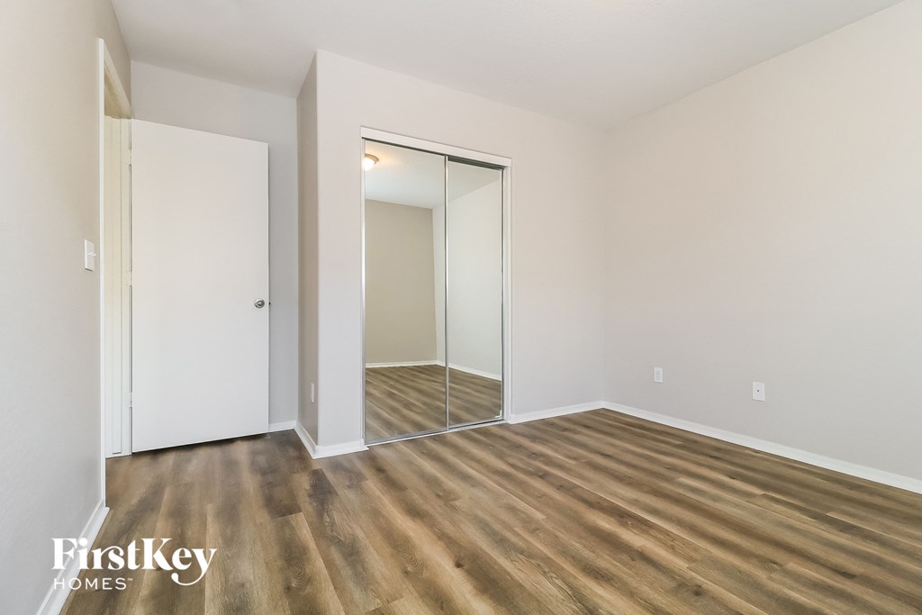 a bedroom with white walls and wood flooring and a mirrored closet