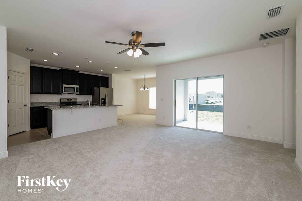 A spacious living room with a ceiling fan and a kitchen area in the background.