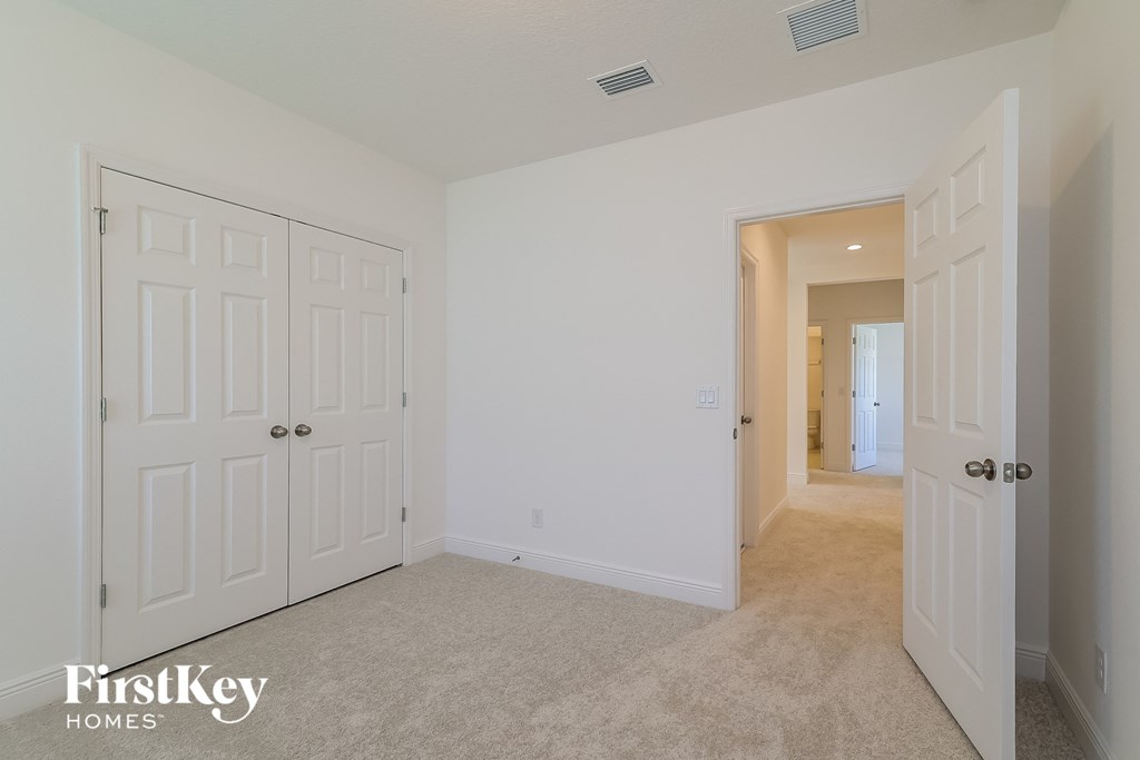 A white bedroom with a carpet floor and a door on the left.